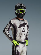 Alpinestars 2026 Racer Lahnd Jersey, jersey de motocross, color Sand Camo con patrón gris y negro, gran logotipo Astars en el pecho, usado con casco negro, gafas y guantes amarillo neón, equipamiento de alto rendimiento para carreras off-road