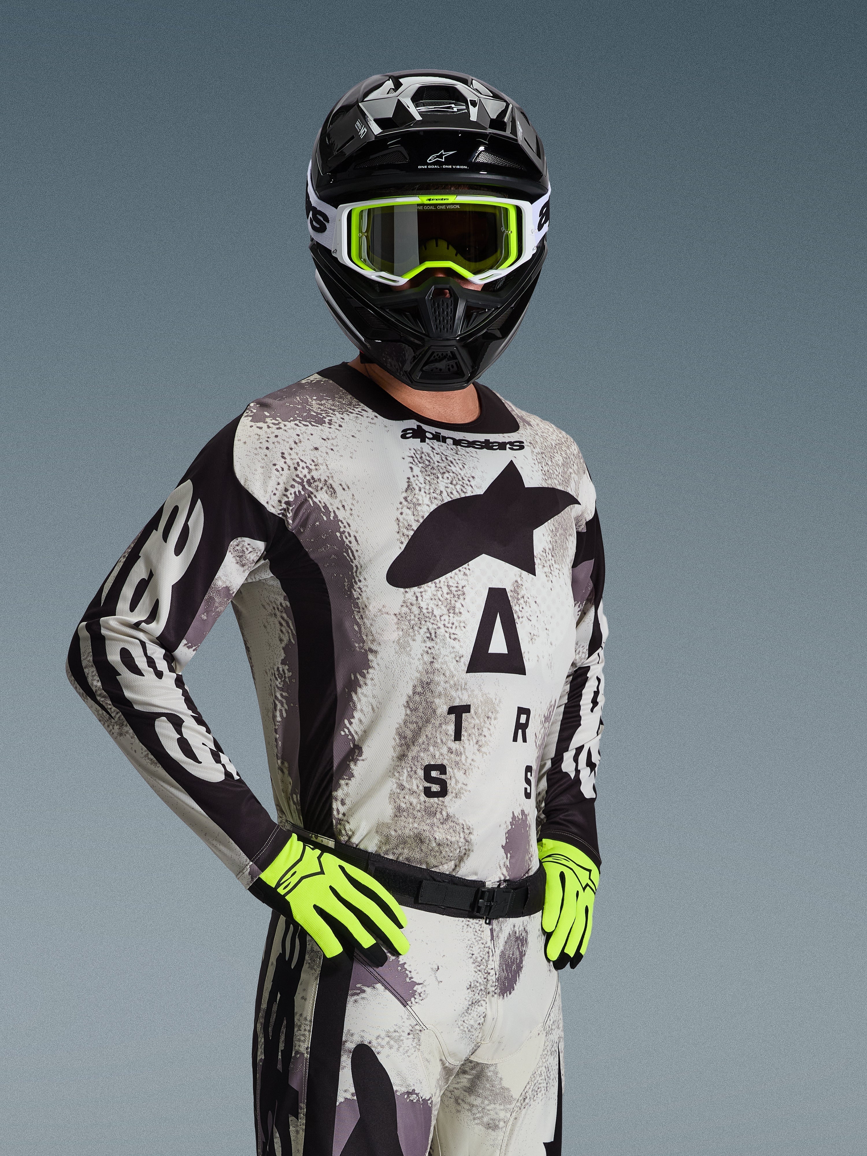 Alpinestars 2026 Racer Lahnd Jersey, jersey de motocross, color Sand Camo con patrón gris y negro, gran logotipo Astars en el pecho, usado con casco negro, gafas y guantes amarillo neón, equipamiento de alto rendimiento para carreras off-road