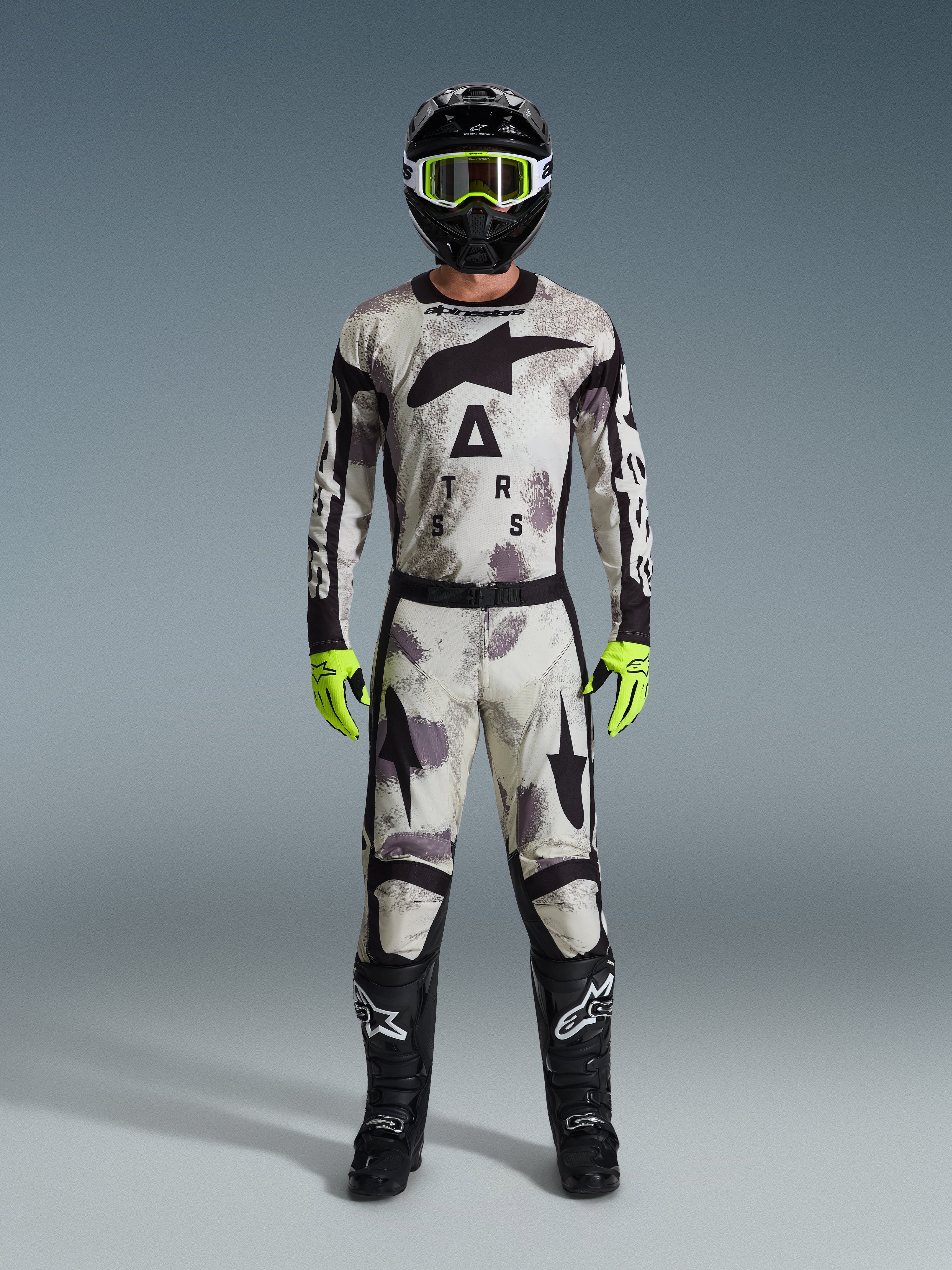 Piloto de motocross con jersey Racer Lahnd 2026 y pantalones a juego en Sand Camo, casco negro con gafas amarillo neón, guantes amarillo neón y botas negras, conjunto completo de equipamiento de carreras off-road de Alpinestars