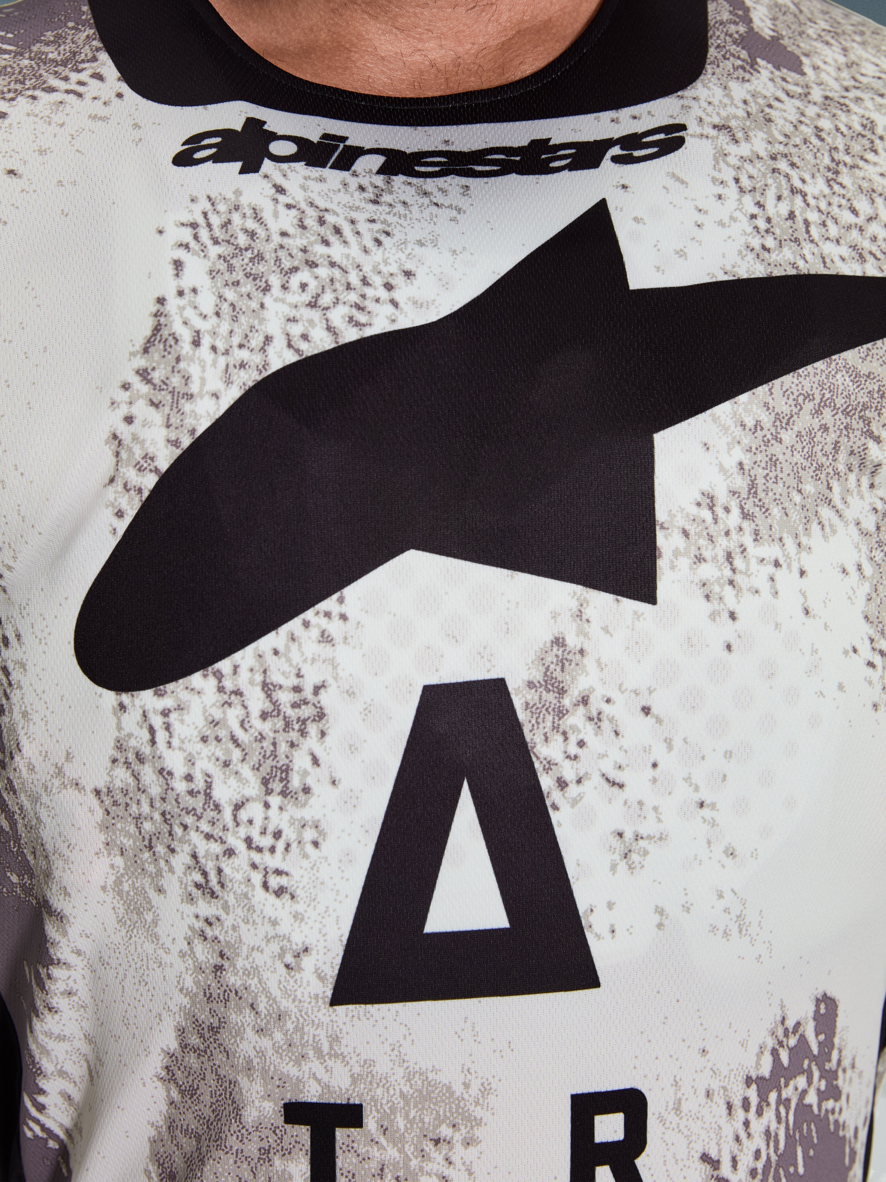 Alpinestars 2026 Racer Lahnd Jersey, primer plano de la zona del pecho, patrón Sand Camo con gran logotipo de estrella negra y marca Alpinestars, polifabricado técnico transpirable para conducción off-road