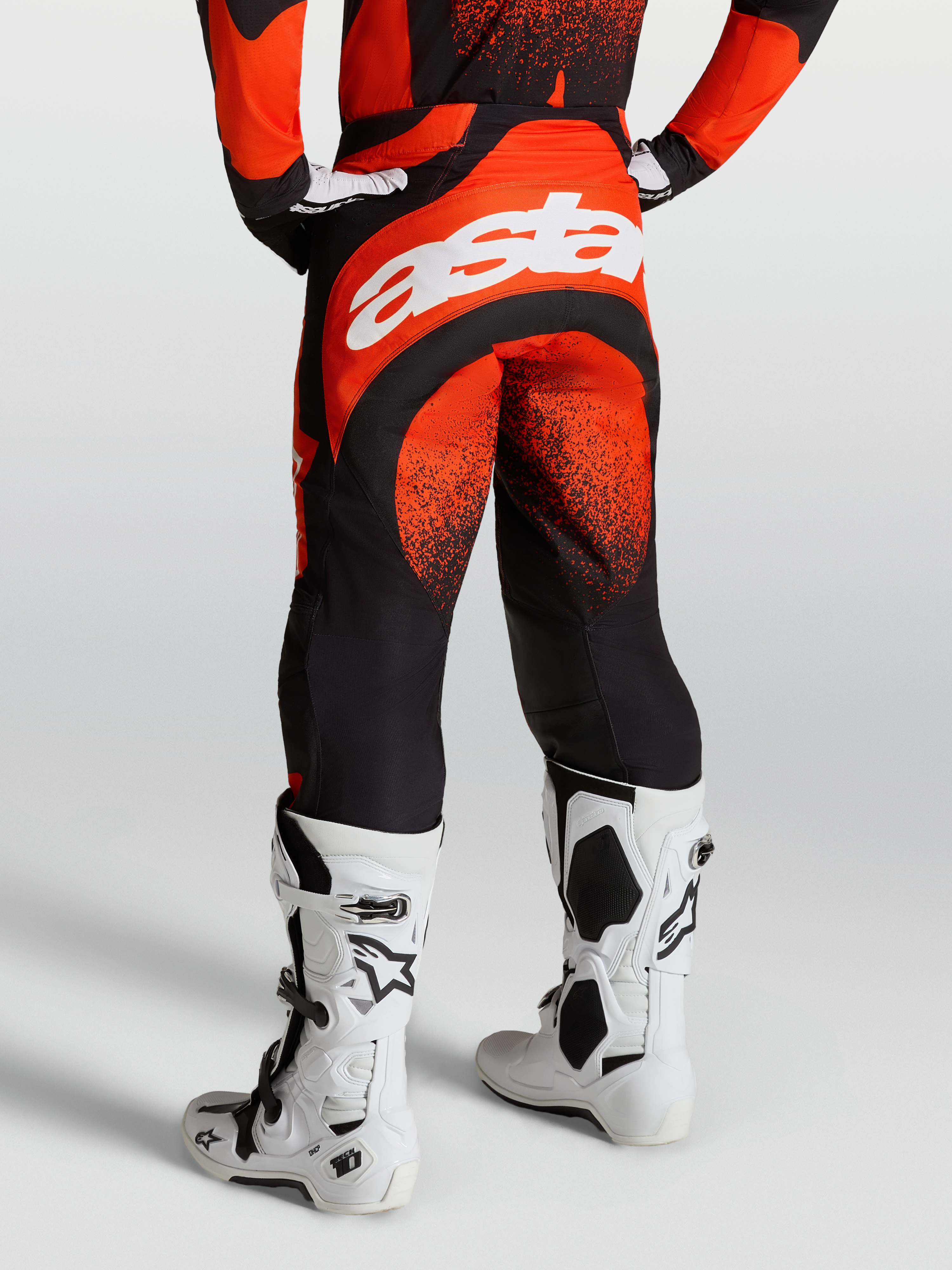Alpinestars Pantalones Techstar Swan, pantalones de motocross para hombre, rojos y negros, chasis elástico duradero con logo Astar blanco, mostrados en modelo con botas Tech 10 blancas