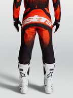 Alpinestars Techstar Swan, pantalones de motocross para hombre, rojos y negros con logo blanco en el asiento, vista trasera en modelo con botas blancas de carreras
