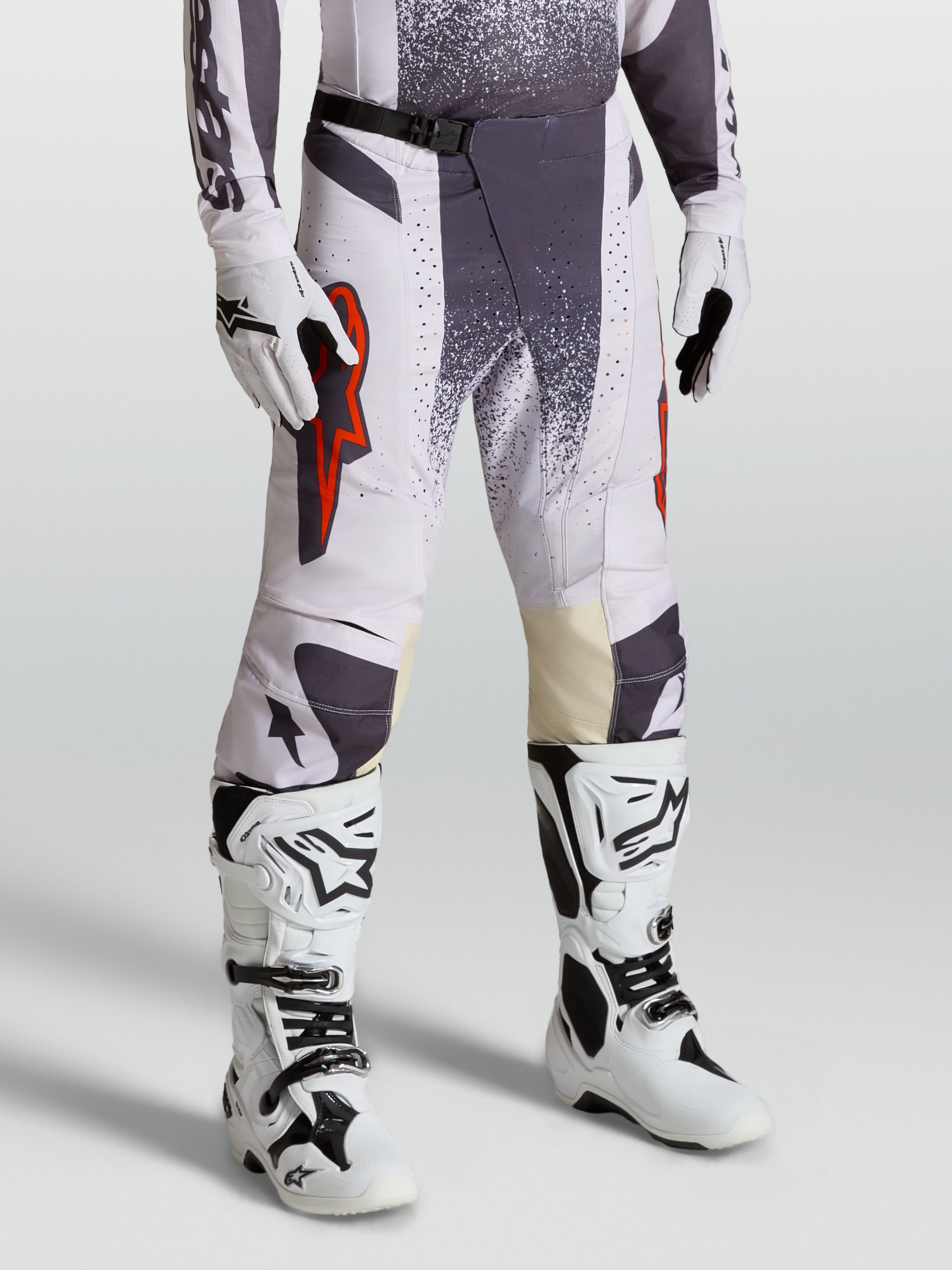 Alpinestars Pantalones Techstar Swan, pantalones de motocross para hombre, lila claro y gris oscuro con detalles en rojo flúor, conjunto con guantes y botas técnicas para competición todoterreno.