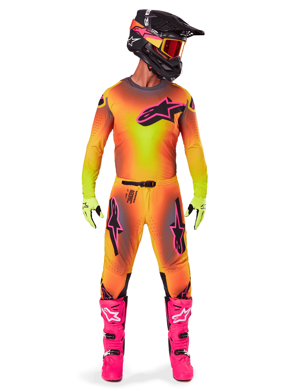 Piloto de motocross con la equipación Alpinestars 2025 Supertech Lipan, con un vibrante diseño degradado en amarillo y rosa, jersey de manga larga a juego, botas rosa brillante, guantes verde lima y casco negro con gafas naranjas.