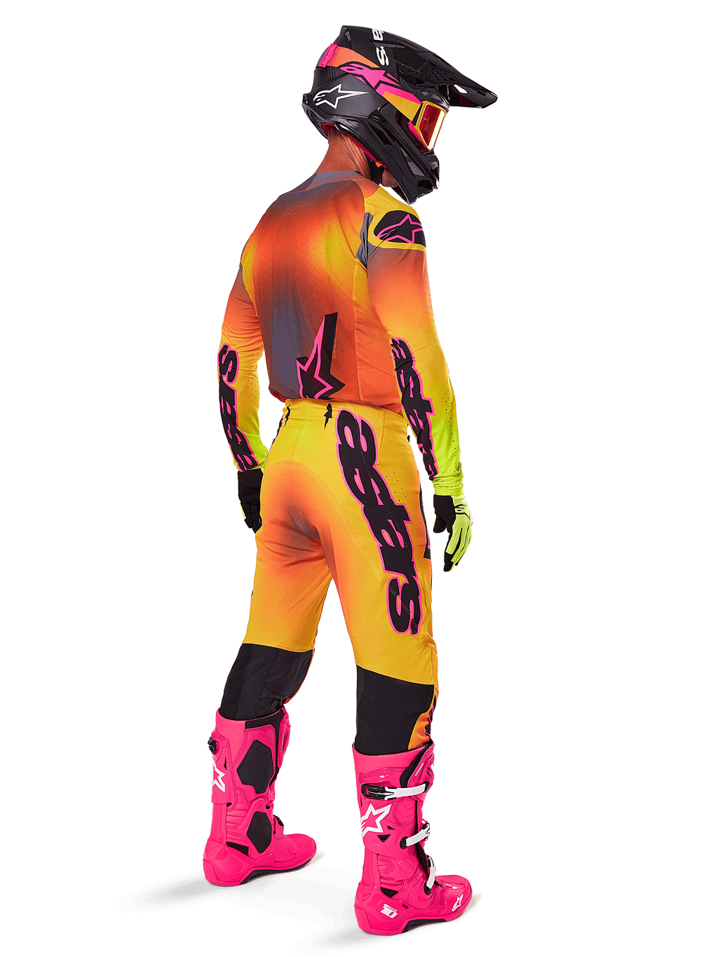 Piloto de motocross visto desde atrás con pantalones Alpinestars 2025 Supertech Lipan en degradado amarillo y rosa, combinado con jersey a juego, botas rosa fucsia y casco negro con detalles rosas, equipamiento profesional coordinado para carreras todoterreno