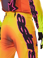 Alpinestars 2025 Supertech Lipan Pants, pantalones de motocross, amarillo y rosa, primer plano de la parte posterior y lateral con llamativos gráficos de Alpinestars en negro y rosa, usados con equipo de carreras a juego