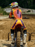 Piloto de motocross visto desde atrás en una parrilla de salida, con pantalones Alpinestars Supertech Lipan 2025 en amarillo y rosa, jersey a juego con detalles rosas y el número 1, botas Alpinestars blancas y casco de carreras, equipo profesional de competición todoterreno coordinado