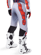 Alpinestars 2025 Supertech Lipan Pants, pantalones de motocross, gris y naranja flúor, vista trasera con un gran gráfico naranja de Alpinestars, paneles elásticos negros, usados con jersey a juego y botas blancas, equipamiento profesional de motocross