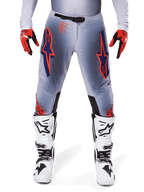 Pantalones Alpinestars Supertech Lipan 2025, pantalones de motocross, gris y naranja fluo, combinados con guantes rojos y negros y botas blancas y negras, con grandes logotipos de estrella de Alpinestars en los muslos y perforaciones de ventilación para carreras de nivel profesional.