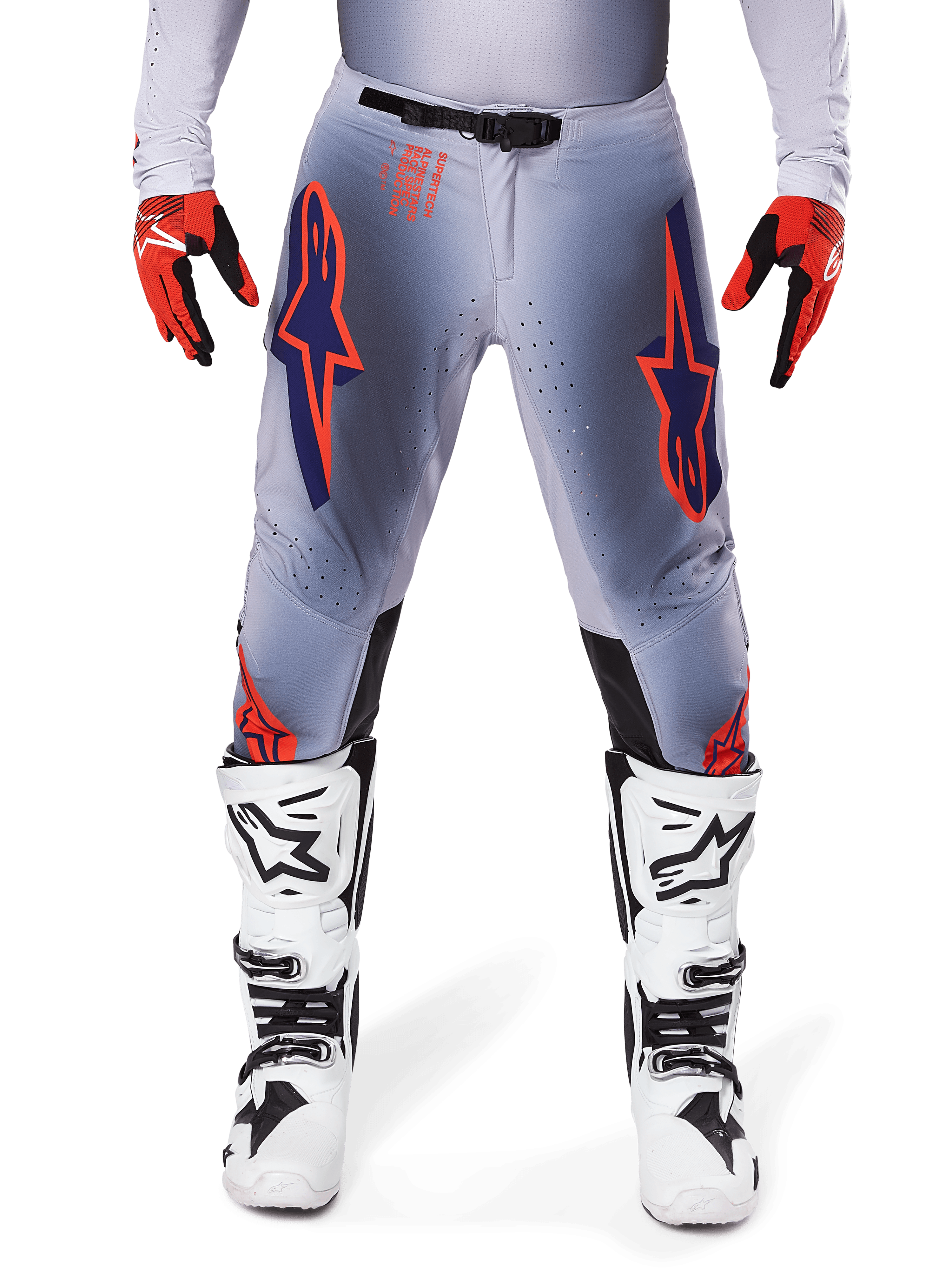 Pantalones Alpinestars Supertech Lipan 2025, pantalones de motocross, gris y naranja fluo, combinados con guantes rojos y negros y botas blancas y negras, con grandes logotipos de estrella de Alpinestars en los muslos y perforaciones de ventilación para carreras de nivel profesional.