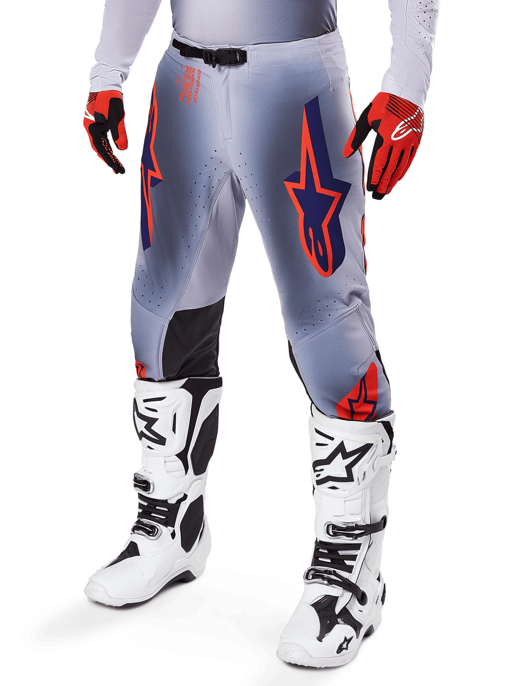 Pantalones Alpinestars Supertech Lipan 2025, pantalones de motocross, gris y naranja flúor, con diseños de estrellas azul marino y paneles interiores negros en las rodillas, usados con guantes rojo anaranjado y botas blancas, equipo profesional de carreras todoterreno
