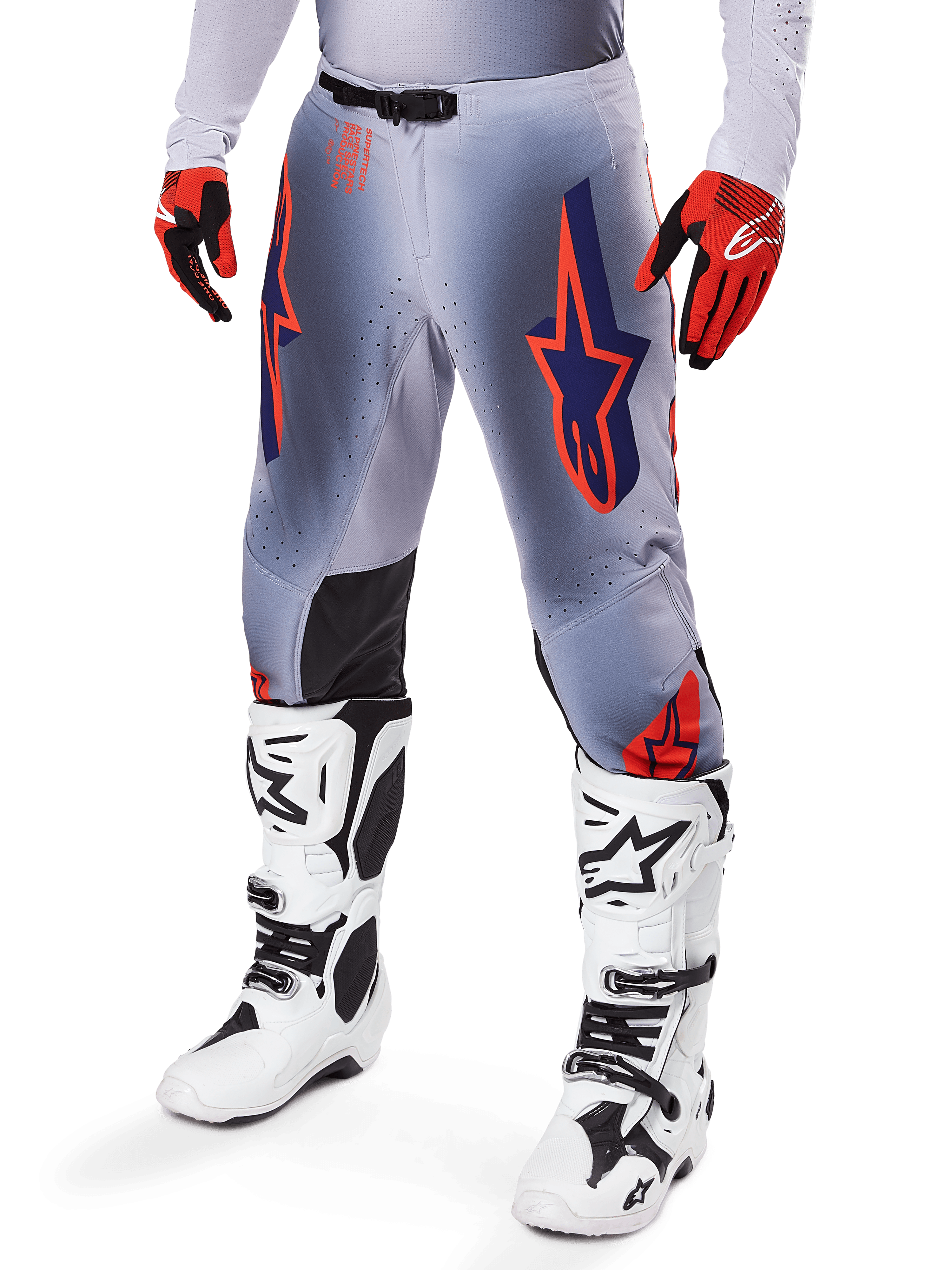 Pantalones Alpinestars Supertech Lipan 2025, pantalones de motocross, gris y naranja flúor, con diseños de estrellas azul marino y paneles interiores negros en las rodillas, usados con guantes rojo anaranjado y botas blancas, equipo profesional de carreras todoterreno