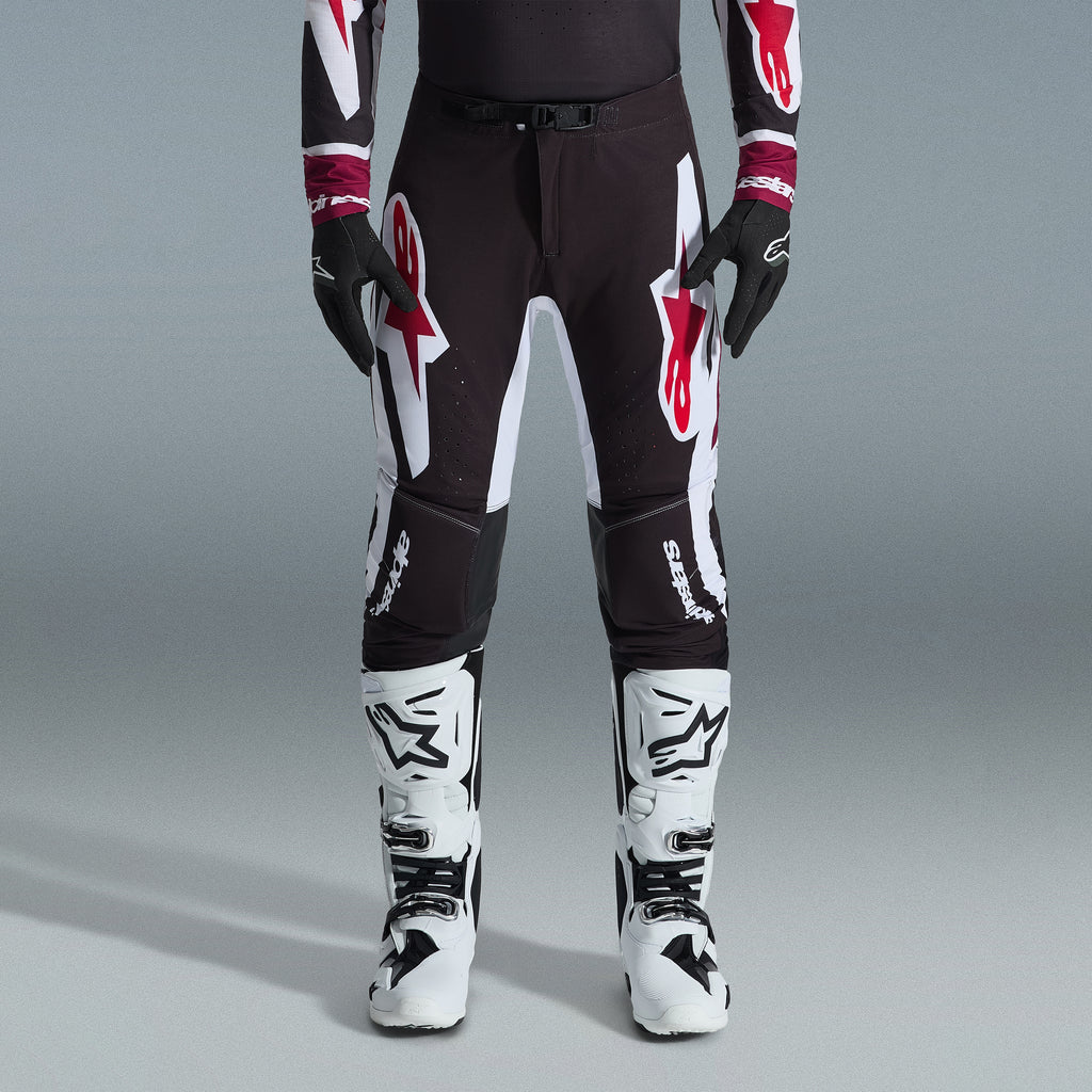 Alpinestars 2026 Supertech AFD Vista Gear Set, Motocross rider wearing black pants with large white and red logos, matching performance jersey with burgundy cuffs, black gloves, and white professional racing boots, high-performance off-road racing outfit