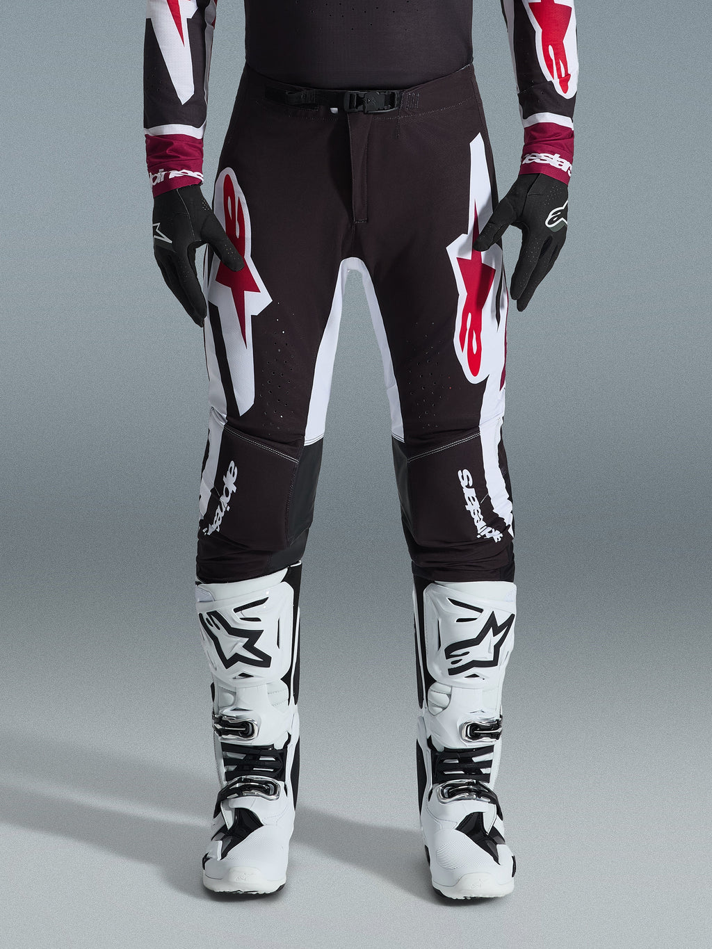 Alpinestars 2026 Supertech AFD Vista Pants, pantalones de motocross, negro, rojo y blanco, con logotipos gráficos grandes en los muslos y las rodillas, combinados con botas de carreras blancas y guantes negros, diseño atlético de competición para competiciones todoterreno de élite