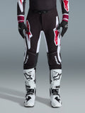 Alpinestars 2026 Supertech AFD Vista Pants, pantalones de motocross, negro, rojo y blanco, con logotipos gráficos grandes en los muslos y las rodillas, combinados con botas de carreras blancas y guantes negros, diseño atlético de competición para competiciones todoterreno de élite
