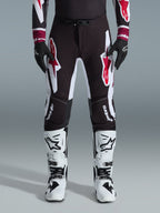 Alpinestars 2026 Supertech AFD Vista Pants, pantalones de motocross, negro, rojo y blanco, con logotipos gráficos grandes en los muslos y las rodillas, combinados con botas de carreras blancas y guantes negros, diseño atlético de competición para competiciones todoterreno de élite
