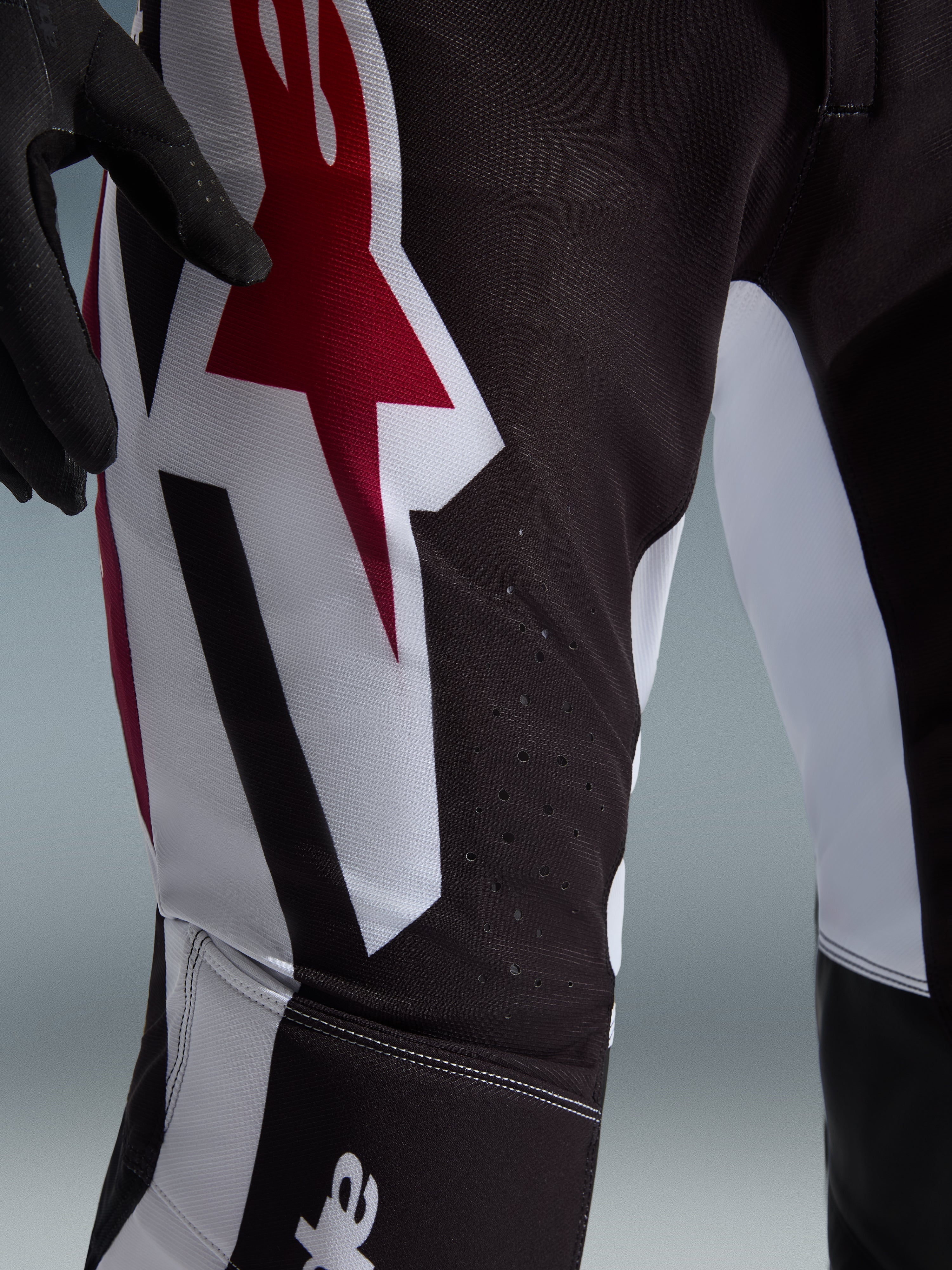 Alpinestars 2026 Supertech AFD Vista Pants, pantalones de motocross, negro, rojo y blanco, primer plano de la zona del muslo con un gran logotipo de estrella en rojo y blanco, perforaciones cortadas con láser para el flujo de aire y tejido ripstop elástico duradero.