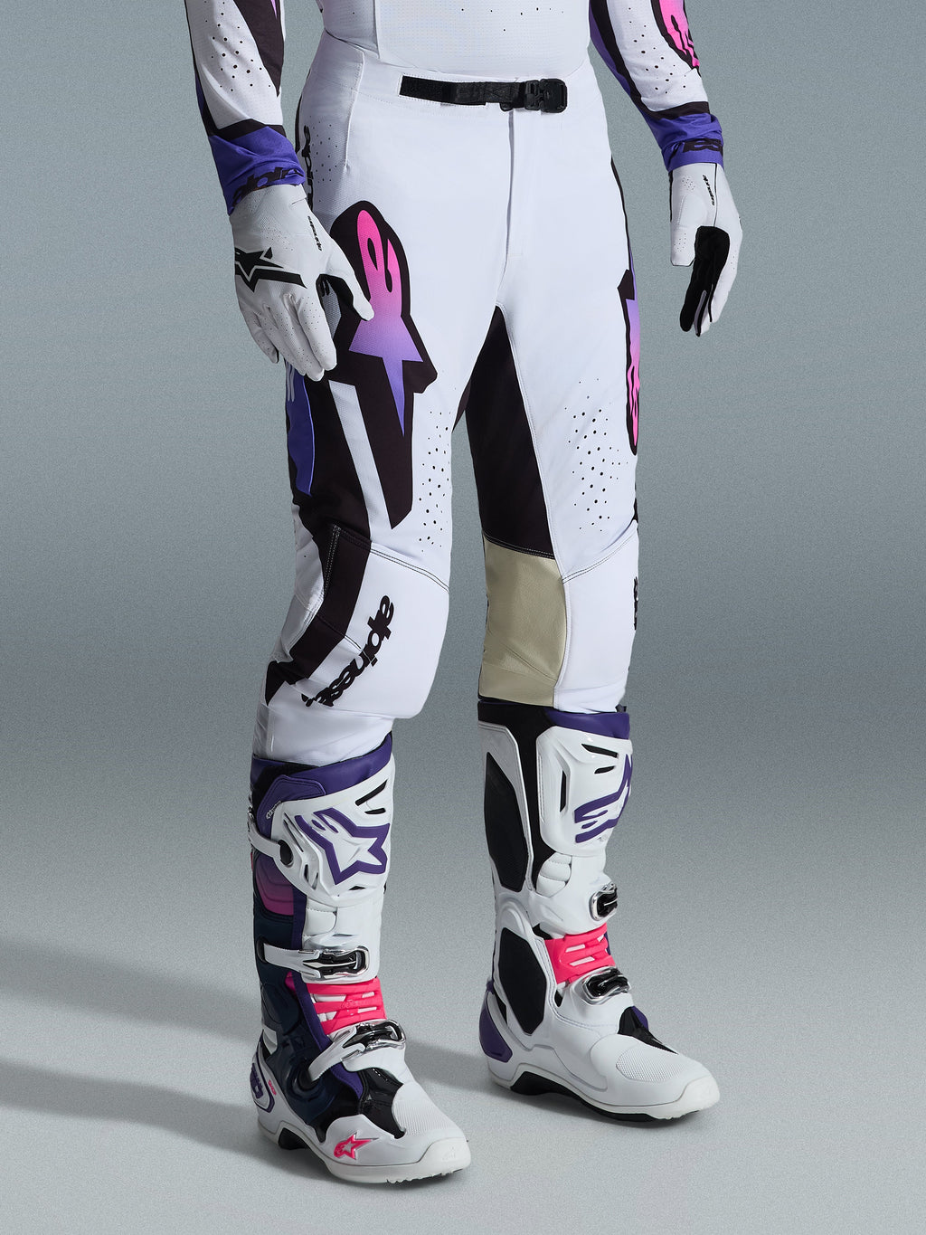 Pantalones Alpinestars Supertech AFD Vista 2026, pantalones de motocross, blancos, morados y negros, con el logotipo Astar en degradado rosa y morado, combinados con botas y guantes de motocross a juego en blanco y morado, ajuste atlético de competición con paneles interiores de las rodillas en cuero tostado y detalles perforados.