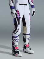 Pantalones Alpinestars Supertech AFD Vista 2026, pantalones de motocross, blancos, morados y negros, con el logotipo Astar en degradado rosa y morado, combinados con botas y guantes de motocross a juego en blanco y morado, ajuste atlético de competición con paneles interiores de las rodillas en cuero tostado y detalles perforados.