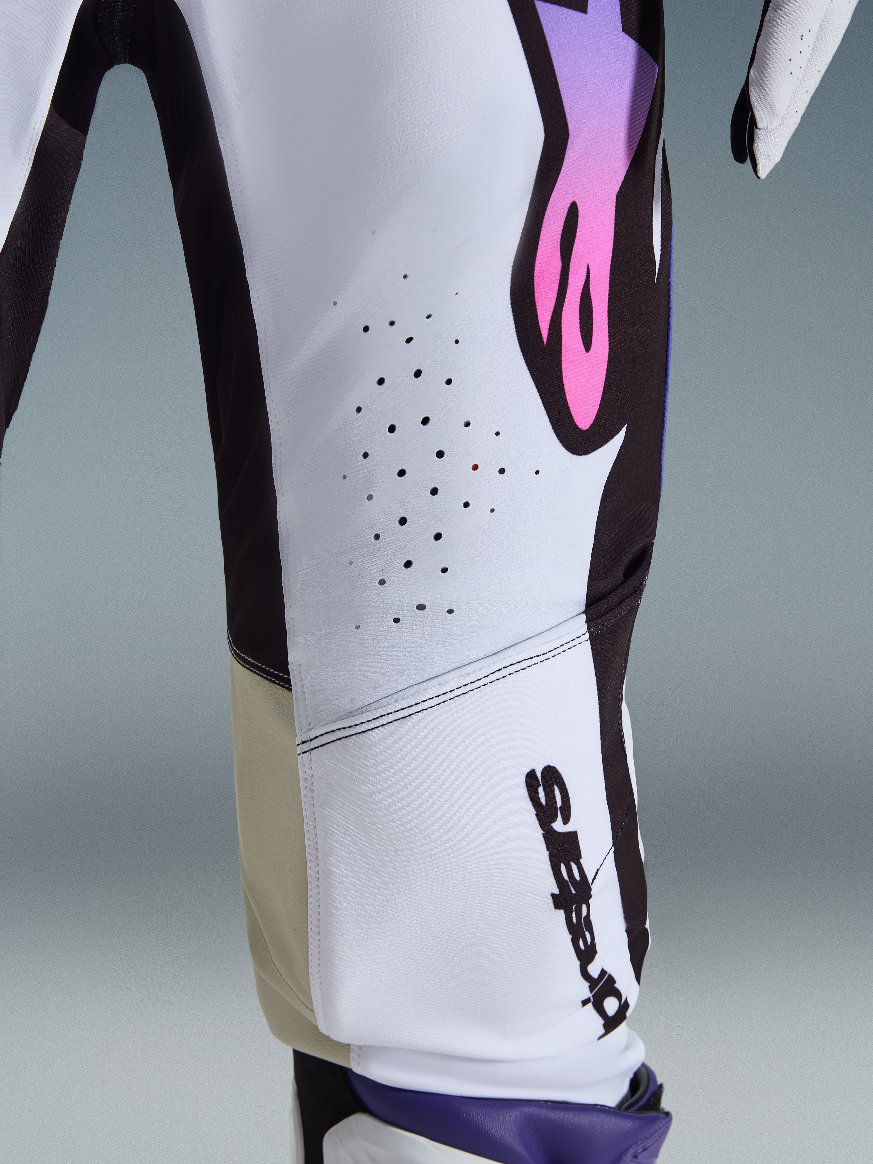 Alpinestars 2026 Supertech AFD Vista Pants, pantalones de motocross, blanco, púrpura y negro, primer plano que muestra las perforaciones de ventilación cortadas con láser, el logotipo vertical de Alpinestars y los paneles interiores de las rodillas en color tostado, equipamiento de competición de alto rendimiento