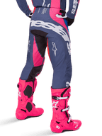 Alpinestars 2025 Techstar Dreem Pants, pantalones de motocross, gris y rosa brillante, combinados con botas rosas a juego, con un gran logotipo blanco de Alpinestars en el asiento y logotipos de estrella en las piernas, ajuste atlético de competición duradero para un alto rendimiento en todoterreno