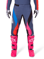 Alpinestars Techstar Dreem Pants 2025, pantalones de motocross, gris multicolor con detalles en rosa, azul y naranja, usados con botas de motocross rosa brillante y jersey a juego, ajuste atlético de competición con perforaciones láser para ventilación