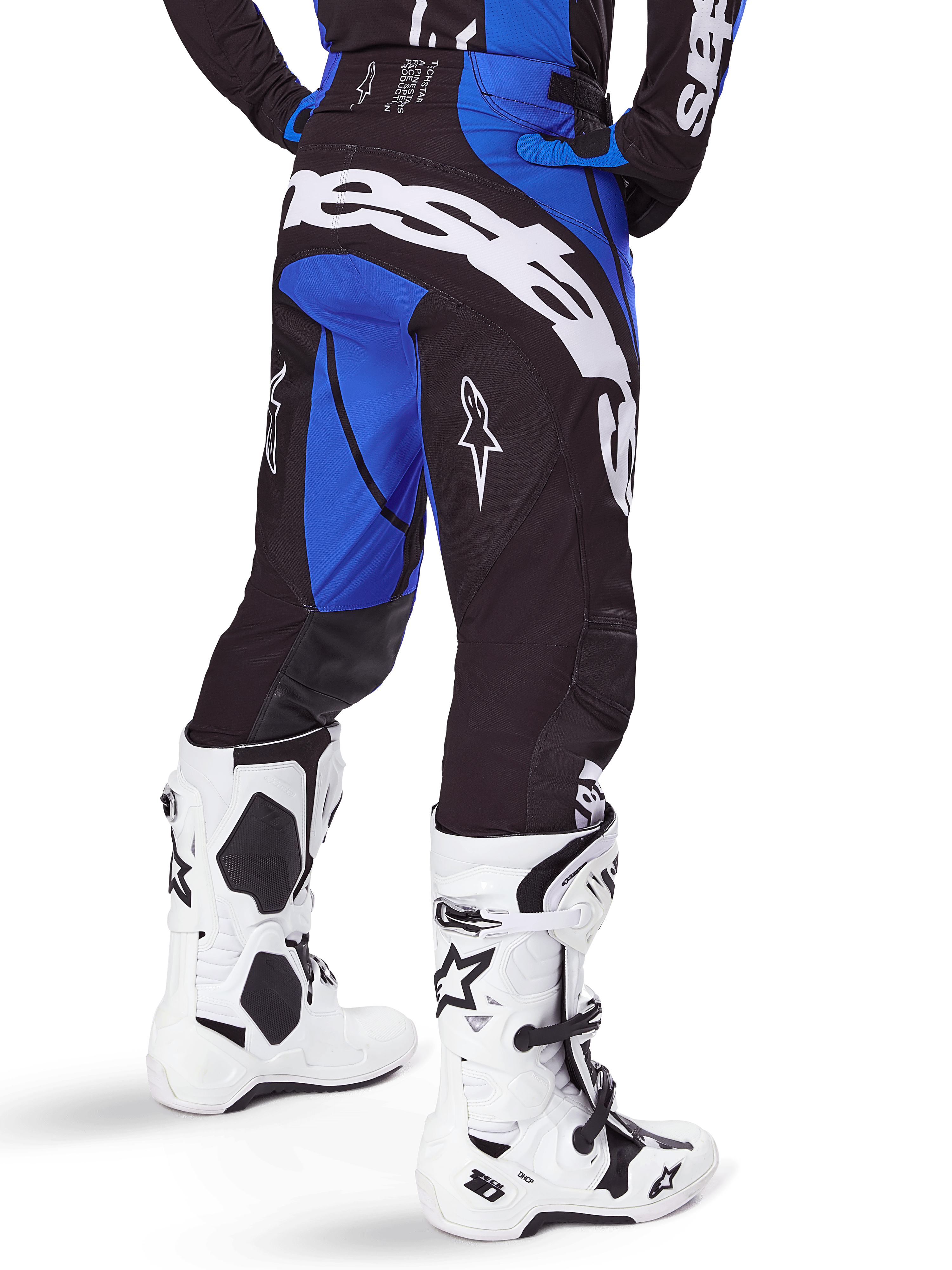 Pantalones Alpinestars Techstar Dreem 2025, pantalones de motocross para hombre, negros y azules, vista trasera con el llamativo logotipo blanco de Alpinestars en el asiento, combinados con botas de motocross blancas y negras y jersey azul a juego, ajuste atlético para competición off-road