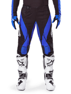 Alpinestars 2025 Techstar Dreem Pants, pantalones de motocross, negros y azules, usados con jersey, guantes a juego y botas blancas, con paneles laterales azules y ajuste atlético de competición, material resistente para carreras off-road