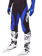 Alpinestars 2025 Techstar Dreem Pants, pantalones de motocross, negros y azules, usados con botas de motocross blancas y guantes azules, con el logo de Alpinestars en blanco en la pierna, construcción duradera para carreras off-road