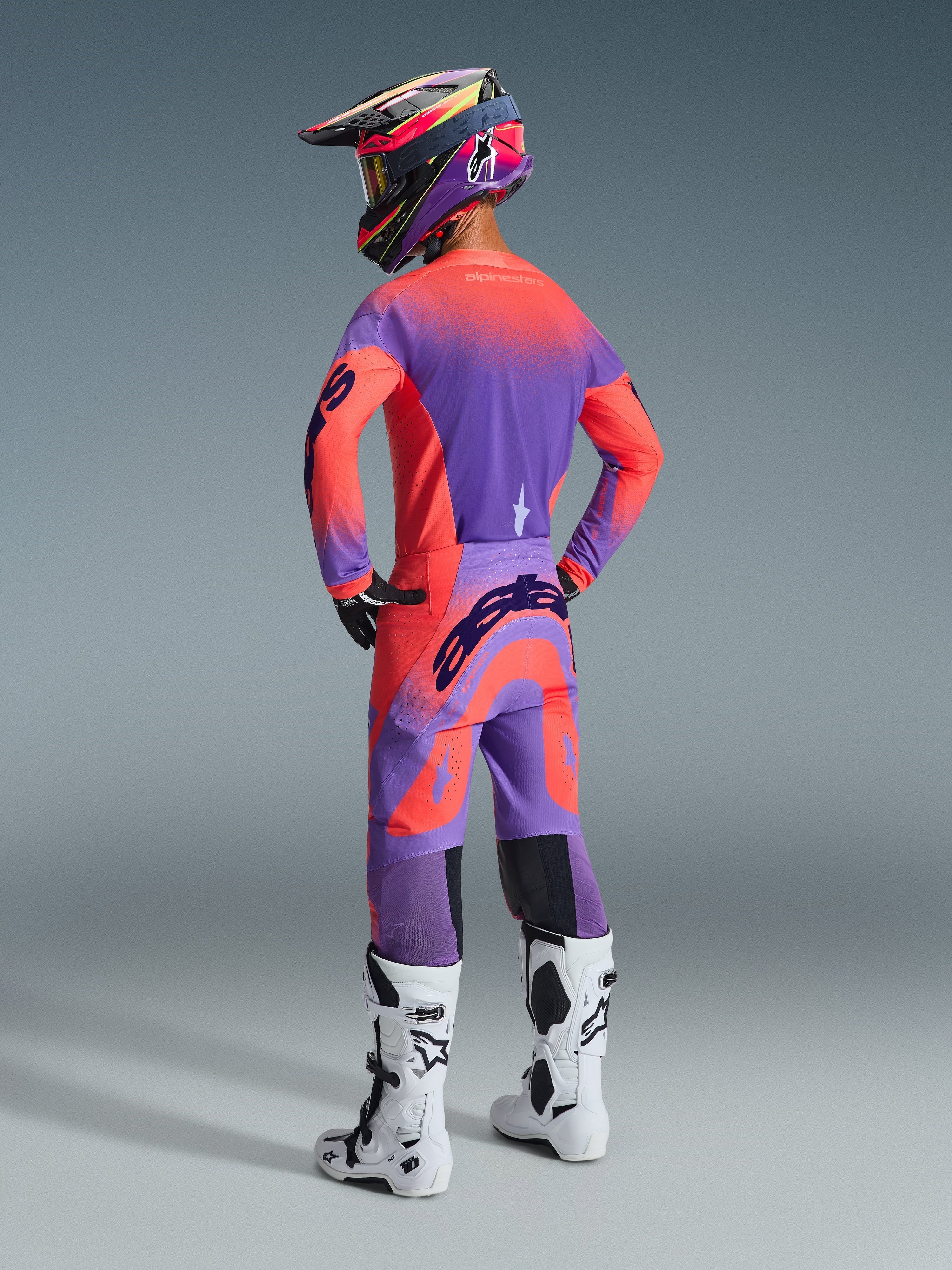 Pantalones Alpinestars Supertech Scenz 2026, pantalones de motocross, coral intenso y púrpura, vista trasera con logotipo llamativo en el asiento, usados por un piloto con jersey a juego y botas blancas, equipo profesional de carreras todoterreno