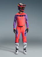 Pantalones Alpinestars Supertech Scenz 2026, pantalones de motocross, color coral brillante y púrpura, usados como un conjunto de equipamiento completo con jersey y casco a juego, botas blancas y negras, con logotipos púrpura y un ajuste atlético de competición.