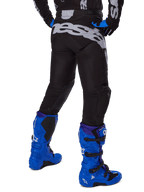 Alpinestars 2025 Racer Graphite Pants, pantalones de motocross, negro y gris, vista trasera con gran marca gris en el asiento, usados con botas de motocross azul brillante y jersey negro y azul, equipamiento de carreras todoterreno duradero