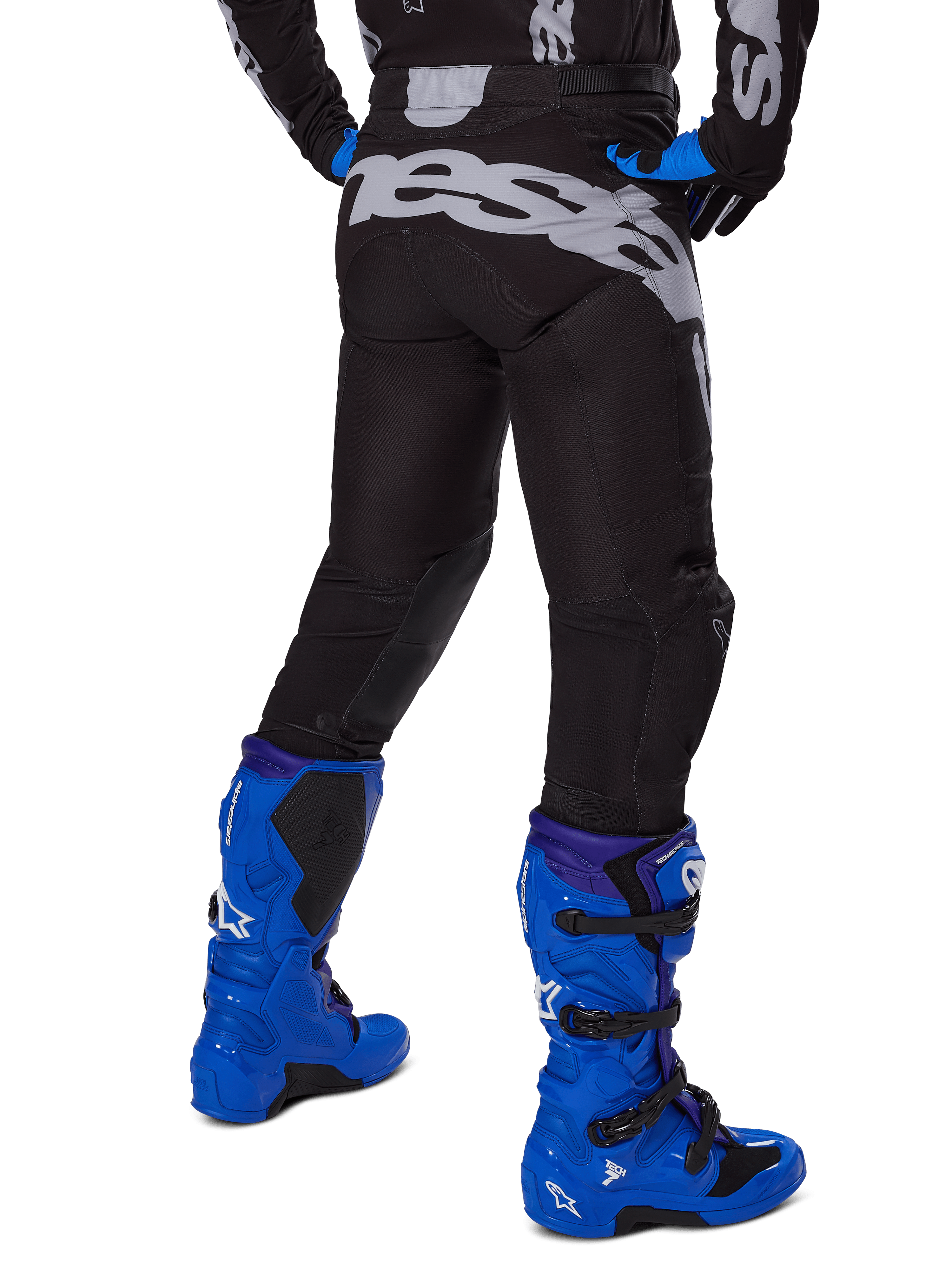 Alpinestars 2025 Racer Graphite Pants, pantalones de motocross, negro y gris, vista trasera con gran marca gris en el asiento, usados con botas de motocross azul brillante y jersey negro y azul, equipamiento de carreras todoterreno duradero
