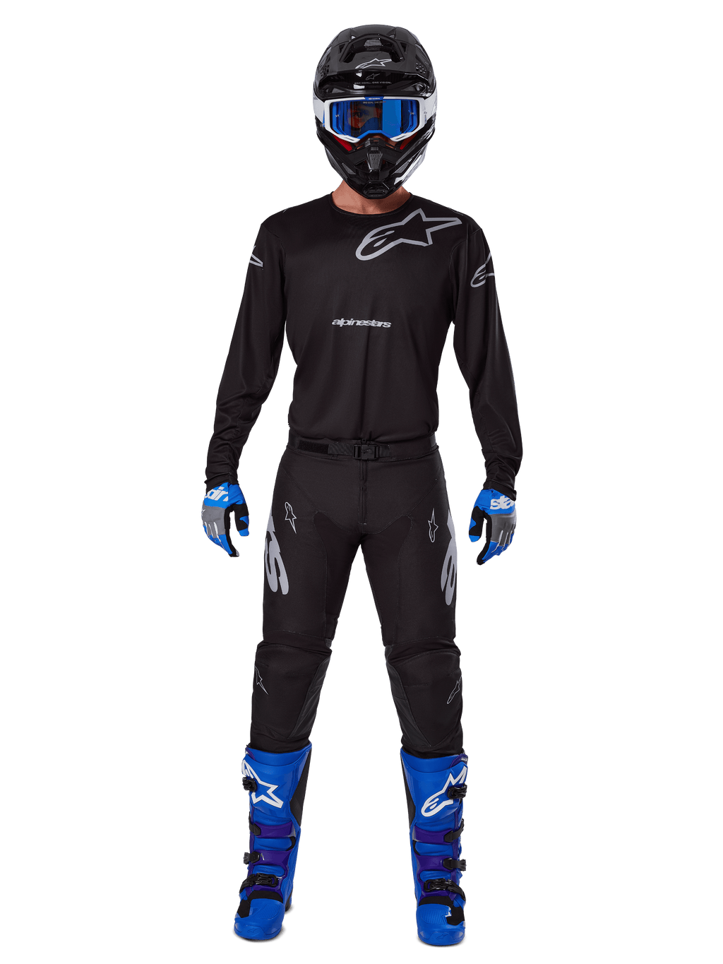 Alpinestars 2025 Racer Graphite Pants, pantalones de motocross, negro y gris, usados por un modelo con un jersey negro a juego, botas azules y moradas, y gafas azules, conjunto completo de carreras off-road con logotipos llamativos de Alpinestars
