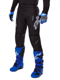 Alpinestars Racer Graphite Pants 2025, pantalones de motocross negros con diseños blancos y grises, combinados con botas de motocross en azul brillante y guantes azules a juego, tejido de alto rendimiento duradero para conducción todoterreno