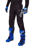 Alpinestars Racer Graphite Pants 2025, pantalones de motocross negros con diseños blancos y grises, combinados con botas de motocross en azul brillante y guantes azules a juego, tejido de alto rendimiento duradero para conducción todoterreno