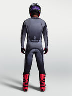 Pantalones Racer Amber de Alpinestars, conjunto de motocross para hombre en gris y lila, vista posterior con botas rojas.