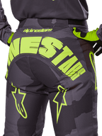 Alpinestars Racer Hollow Pants 2025, pantalones de motocross, camuflaje oscuro y amarillo flúor, con un gran logotipo de Alpinestars en amarillo en la parte trasera, patrón de camuflaje táctico con detalles en amarillo vibrante y construcción duradera para carreras off-road.
