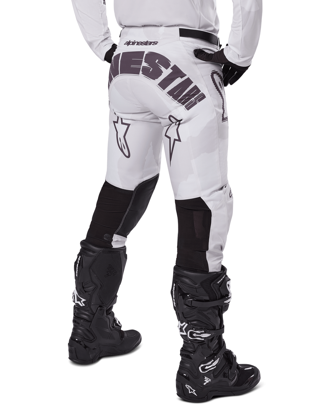 Alpinestars 2025 Racer Hollow Pants, pantalones de motocross, marrón camuflaje claro, vista trasera del piloto que muestra el gran logotipo en el asiento y paneles elásticos negros en la parte inferior de las piernas, combinados con botas Tech 7 negras