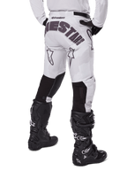 Alpinestars 2025 Racer Hollow Pants, pantalones de motocross, marrón camuflaje claro, vista trasera del piloto que muestra el gran logotipo en el asiento y paneles elásticos negros en la parte inferior de las piernas, combinados con botas Tech 7 negras