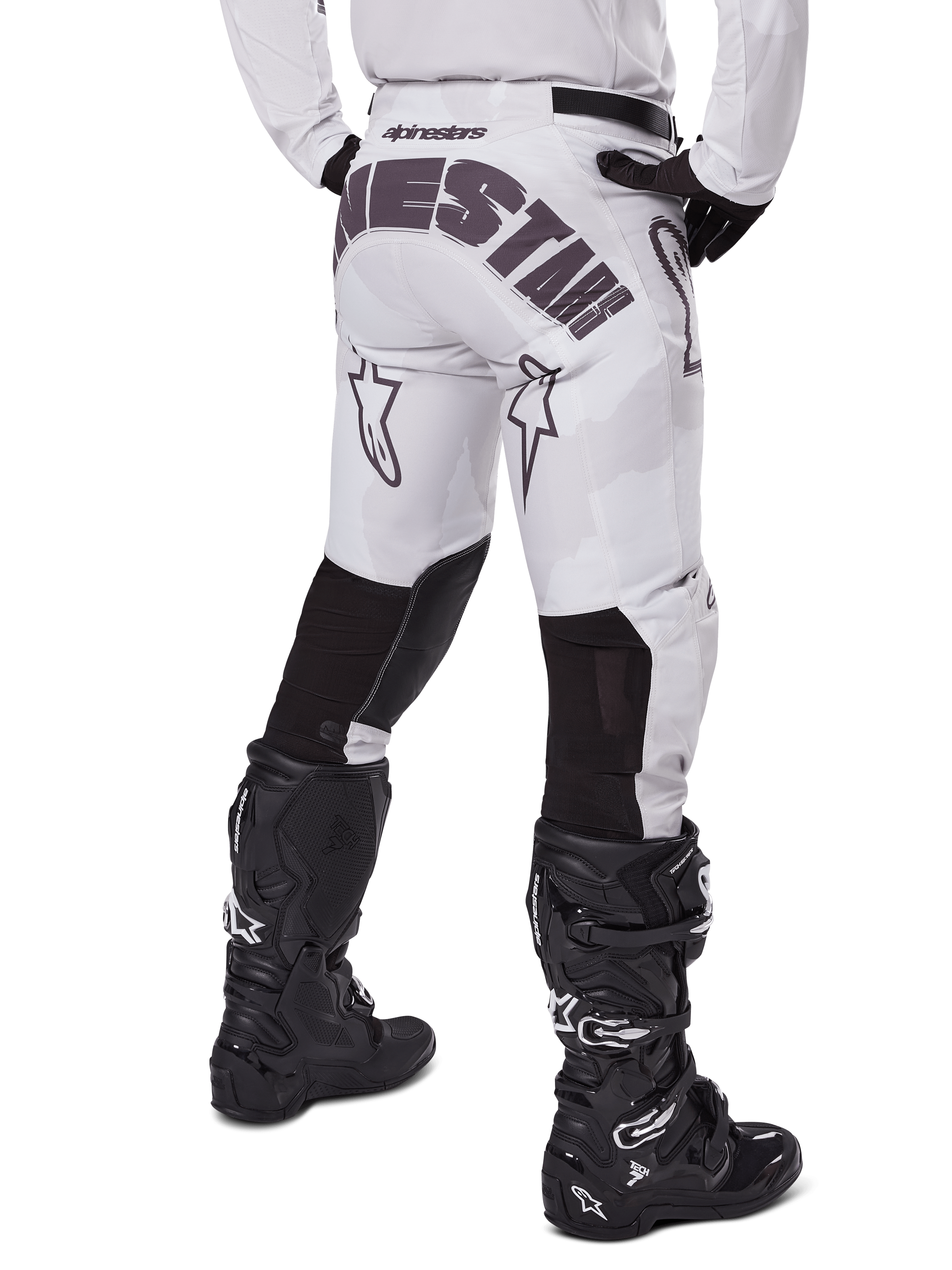 Alpinestars 2025 Racer Hollow Pants, pantalones de motocross, marrón camuflaje claro, vista trasera del piloto que muestra el gran logotipo en el asiento y paneles elásticos negros en la parte inferior de las piernas, combinados con botas Tech 7 negras