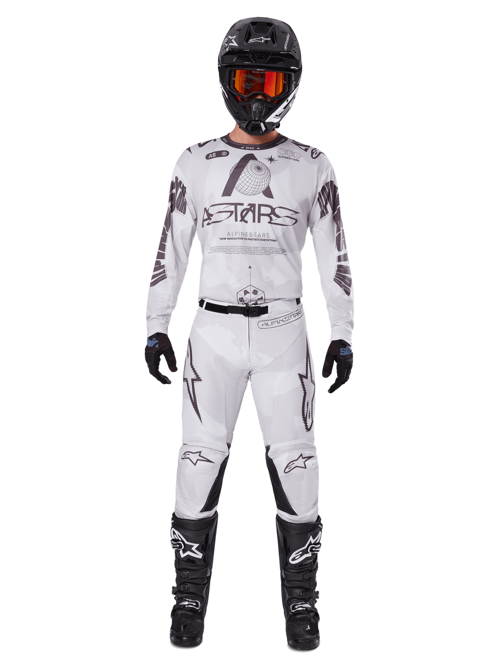 Piloto de motocross con los pantalones Alpinestars 2025 Racer Hollow en color Light Camo Brown, combinados con un jersey de manga larga a juego en blanco y gris, casco negro con gafas de color rojo anaranjado, guantes negros y botas negras, conjunto de equipamiento de carreras coordinado para rendimiento off-road.