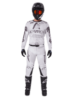 Piloto de motocross con los pantalones Alpinestars 2025 Racer Hollow en color Light Camo Brown, combinados con un jersey de manga larga a juego en blanco y gris, casco negro con gafas de color rojo anaranjado, guantes negros y botas negras, conjunto de equipamiento de carreras coordinado para rendimiento off-road.