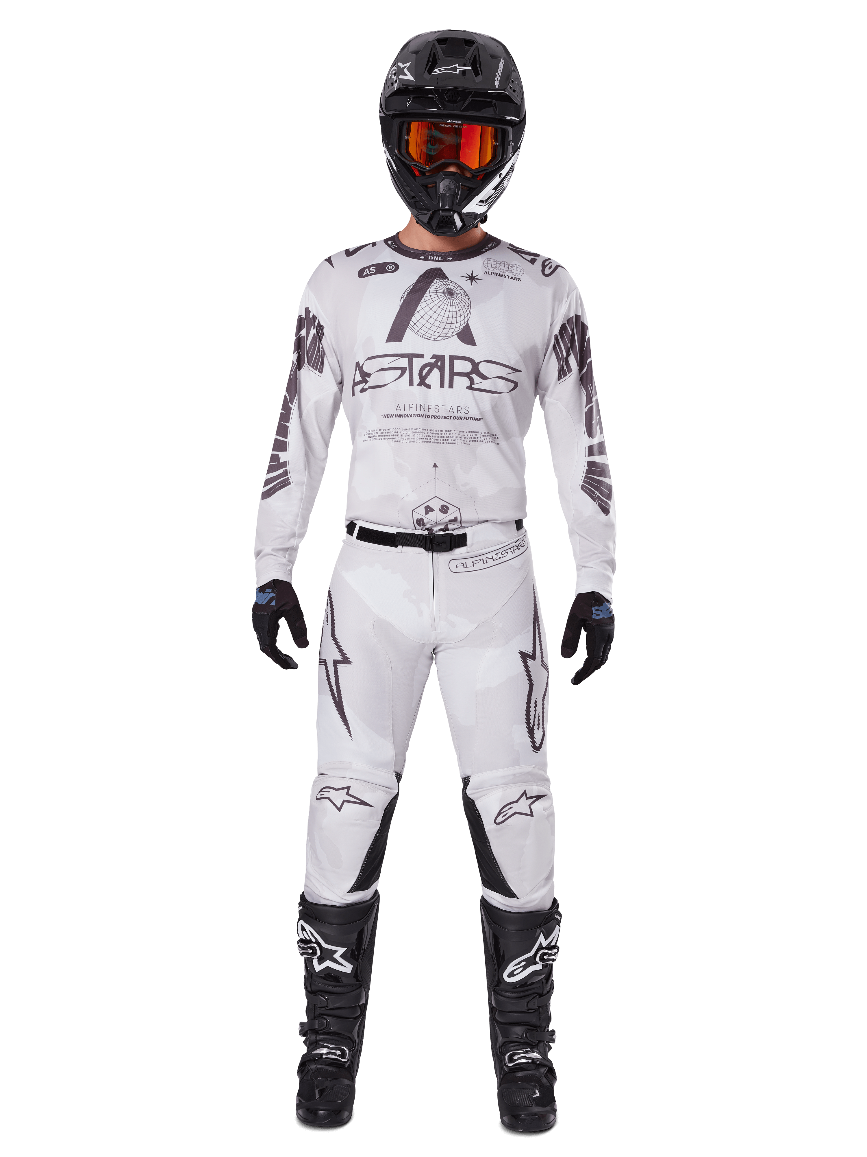 Piloto de motocross con los pantalones Alpinestars 2025 Racer Hollow en color Light Camo Brown, combinados con un jersey de manga larga a juego en blanco y gris, casco negro con gafas de color rojo anaranjado, guantes negros y botas negras, conjunto de equipamiento de carreras coordinado para rendimiento off-road.
