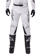 Alpinestars 2025 Racer Hollow Pants, pantalones de motocross, marrón camuflaje claro, usados con guantes negros y botas de motocross, con un sutil patrón de camuflaje, gráficos negros y logotipos Astars, diseño ergonómico para conducción off-road