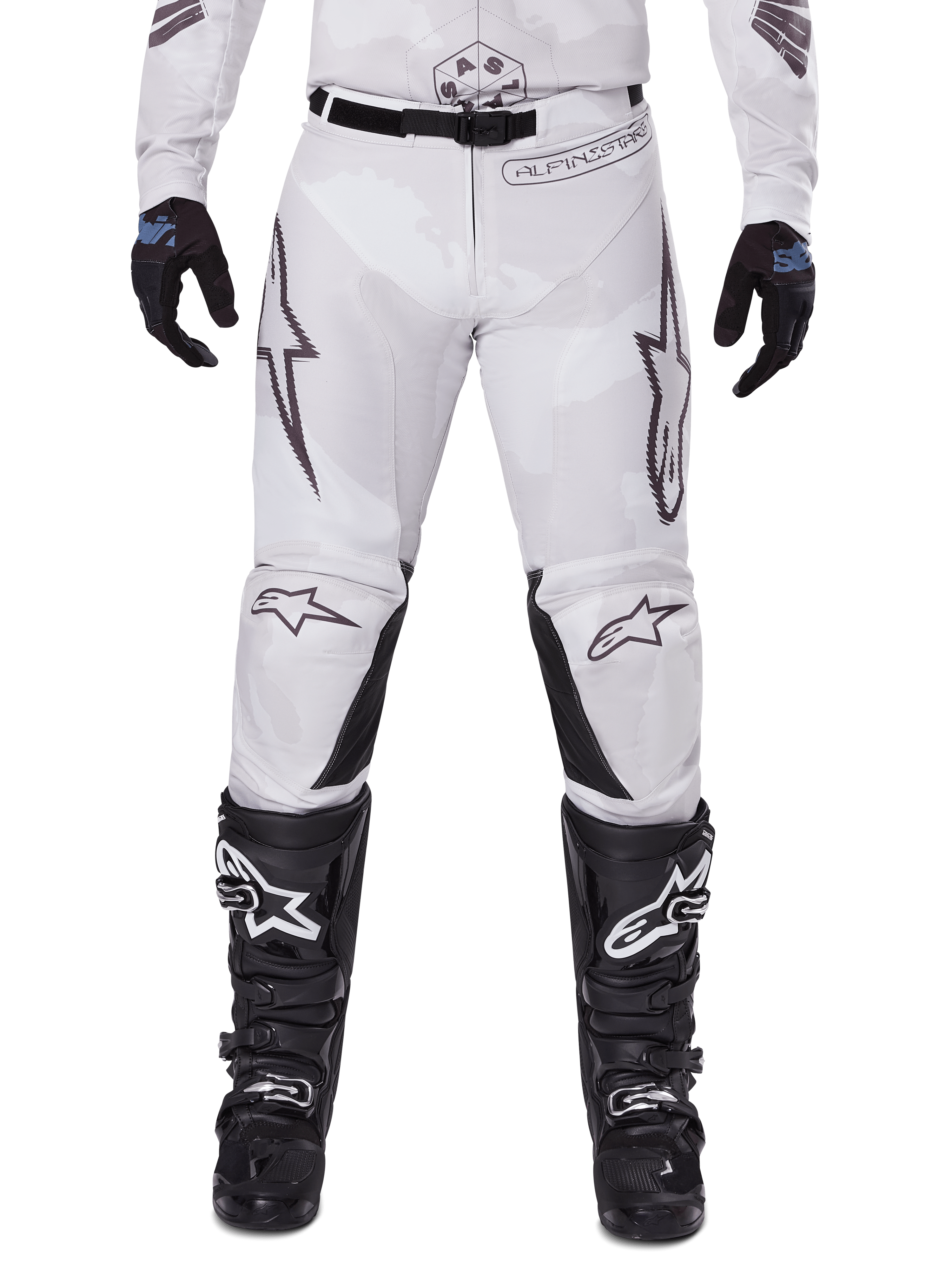 Alpinestars 2025 Racer Hollow Pants, pantalones de motocross, marrón camuflaje claro, usados con guantes negros y botas de motocross, con un sutil patrón de camuflaje, gráficos negros y logotipos Astars, diseño ergonómico para conducción off-road