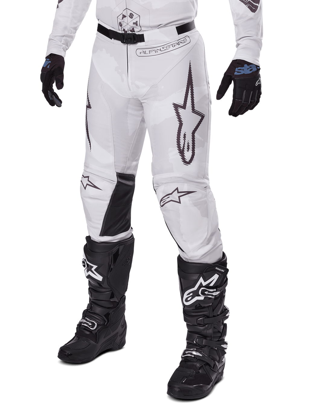 Alpinestars 2025 Racer Hollow Pants, pantalones de motocross, camuflaje blanco y gris, con grandes logotipos de estrellas contorneados en negro y paneles interiores de cuero negro en las rodillas, usados con botas y guantes de motocross negros, diseño duradero para carreras off-road.