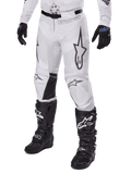Alpinestars 2025 Racer Hollow Pants, pantalones de motocross, camuflaje blanco y gris, con grandes logotipos de estrellas contorneados en negro y paneles interiores de cuero negro en las rodillas, usados con botas y guantes de motocross negros, diseño duradero para carreras off-road.