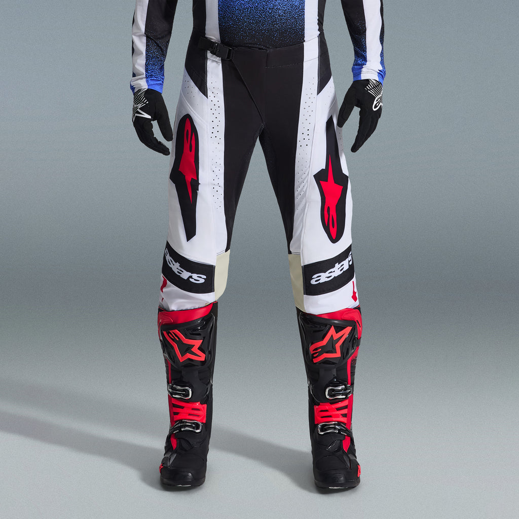 Alpinestars 2026 Techstar Knif Gear Set, equipamiento de motocross, pantalones negros y blancos con logotipos de estrellas rojas grandes, usados con botas de carreras negras y rojas y guantes negros, ajuste atlético profesional para rendimiento todoterreno