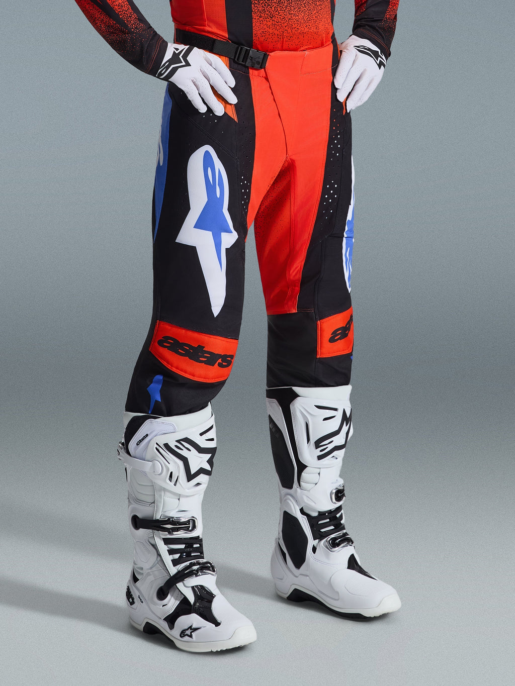 Alpinestars 2026 Techstar Knif Pants, pantalones de motocross, color naranja, negro y azul UCLA, combinados con guantes blancos y botas de motocross blancas y negras, con logotipos llamativos en los muslos y paneles naranjas en las rodillas con la marca astars.